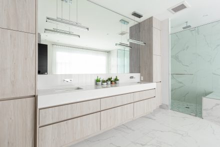 Meubles de salle de bain moderne avec armoires claires et douche en verre.
