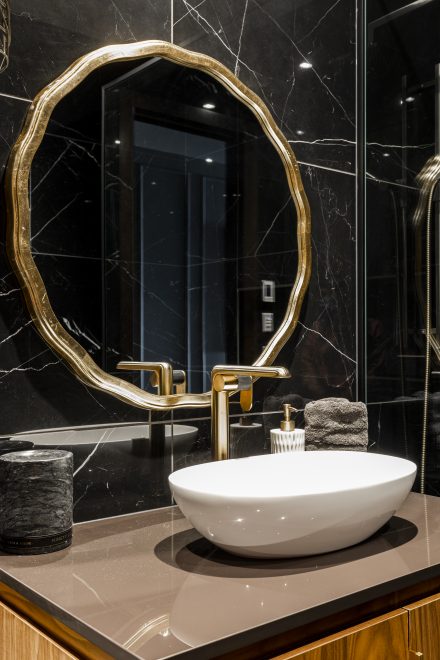 Salle de bain foncée avec miroir et robinet à l'allure dorée.